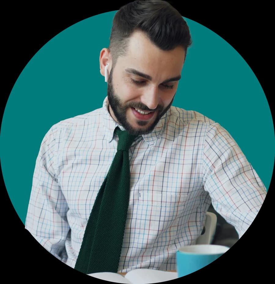 A smiling man with an earbud reads at his desk.